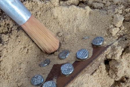 photo of sand being brushed away to reveal a metal object.