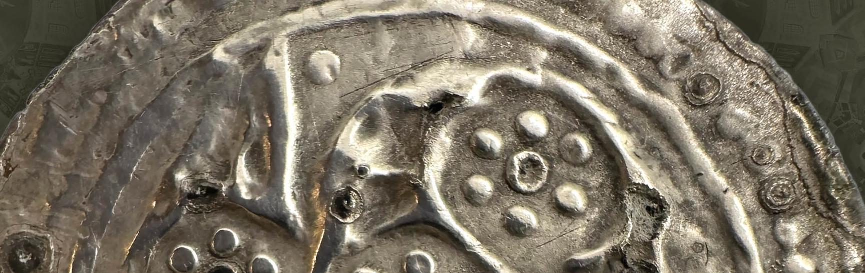 close up photo of ancient silver coin with decorative design of dots and spirals.
