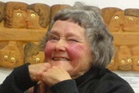 photo of old woman smiling in front of wood carving