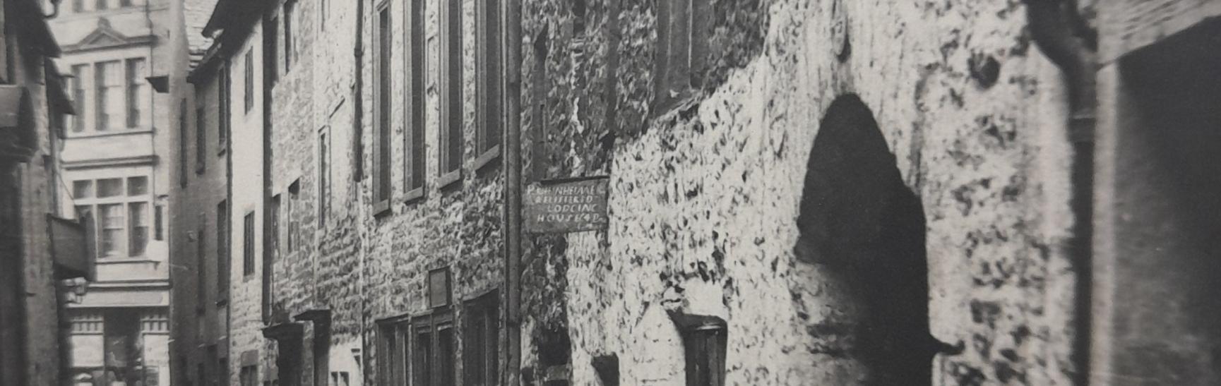 old photo of stone building in narrow street with sign advertising rooms