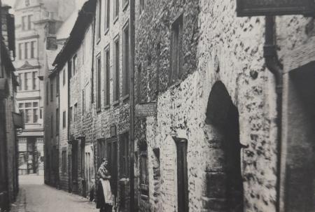 old photo of stone building in narrow street with sign advertising rooms